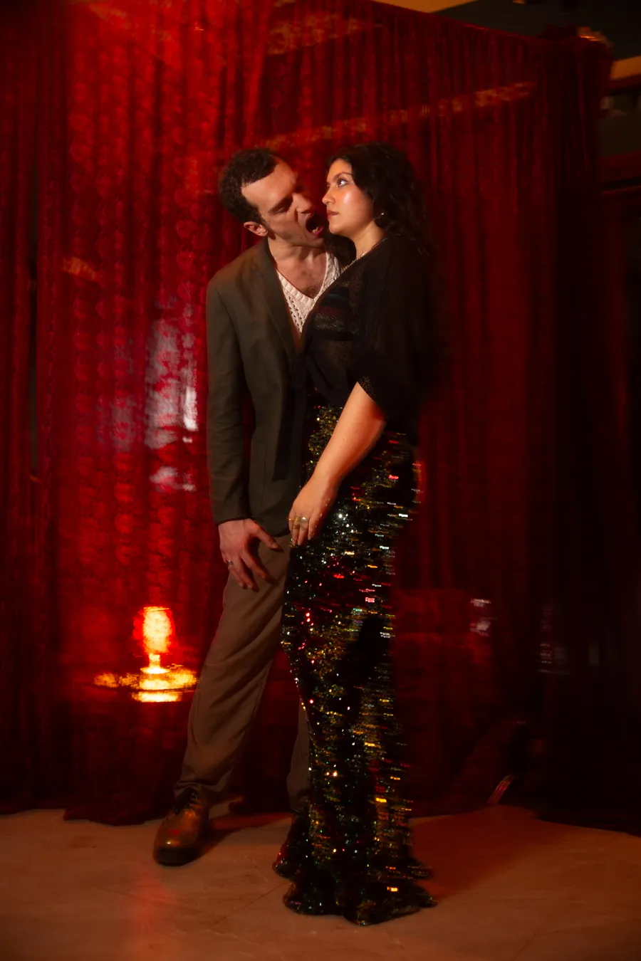 Person in a black bodysuit and dance shoes arching backward in a tiled foyer beside a standing mirror.