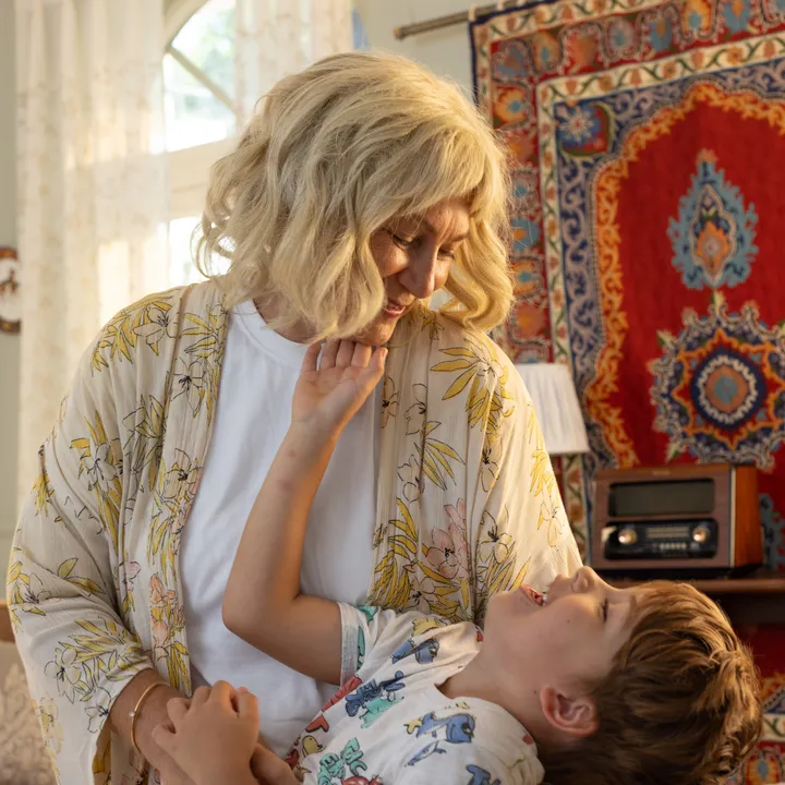 Dolaren project cover — older woman and young boy laughing together in a sunlit room with patterned wallpaper.