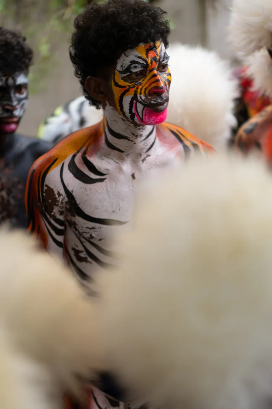 Performer with orange, white, and black tiger-inspired body painting viewed between white furry headpieces.
