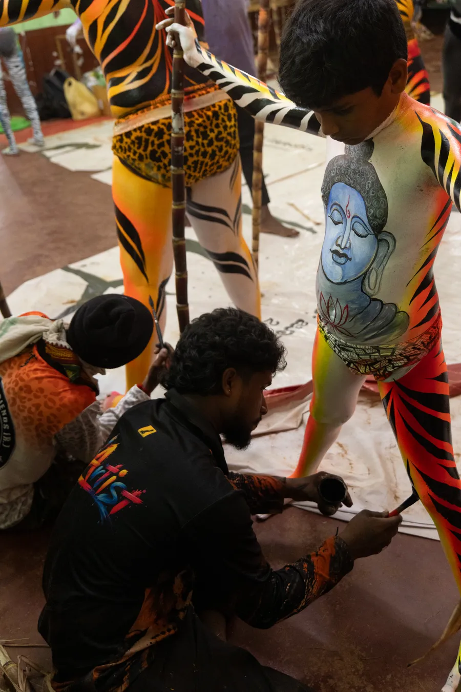 Artist paints the lower leg of a performer whose torso features a blue painted figure.