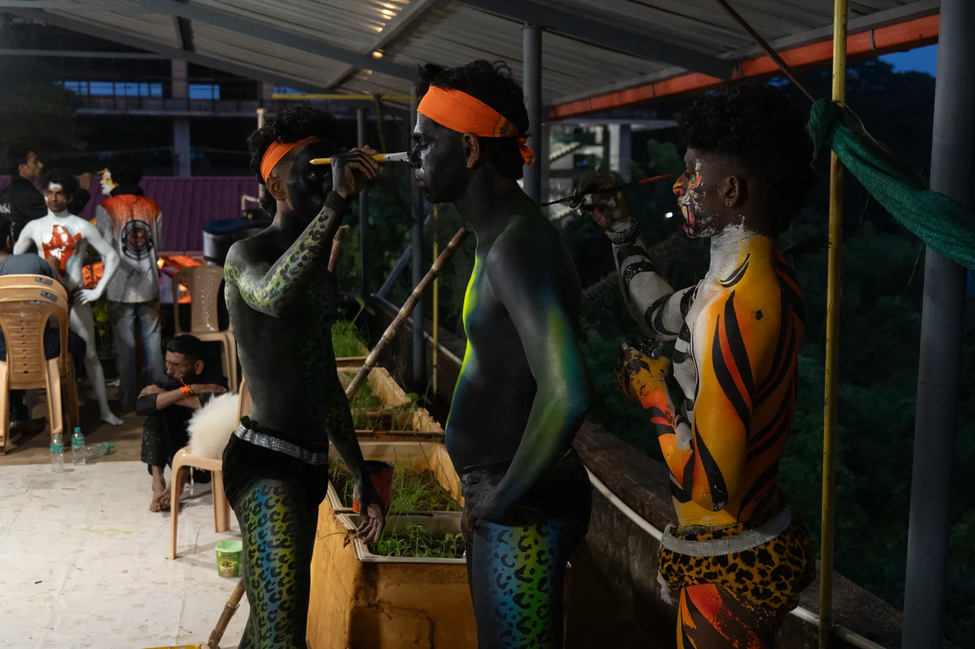 Two artists apply face paint to black-painted and tiger-striped performers outdoors.