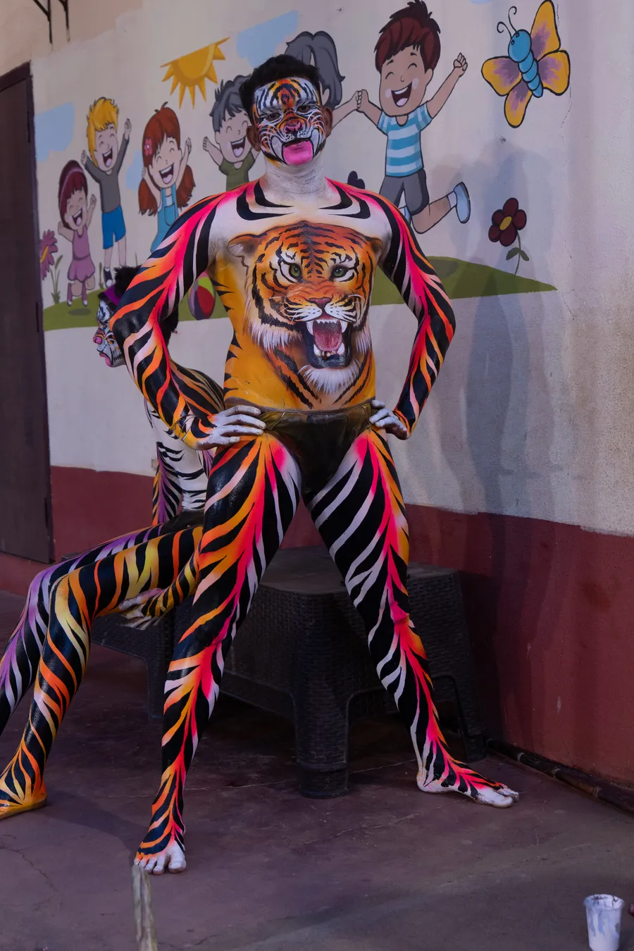 Tiger-striped performer stands with hands on hips, showing a large painted tiger face across the torso.