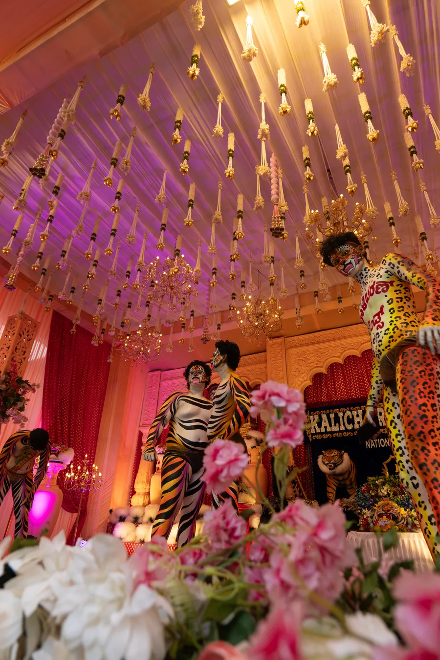 Low-angle view of tiger-striped and spotted performers on a decorated stage beneath hanging floral garlands.