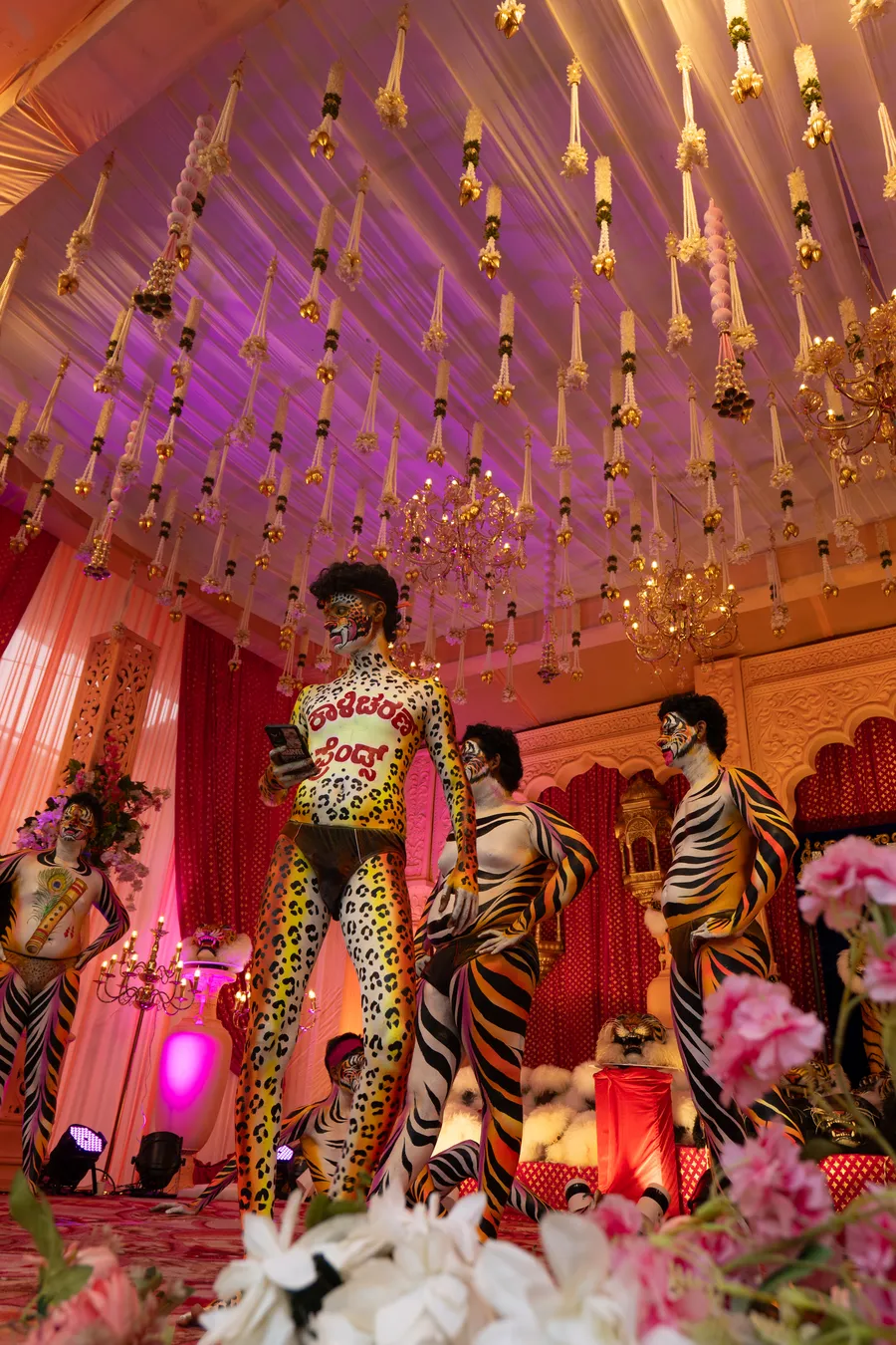 Spotted and tiger-striped performers stand beneath chandeliers and hanging floral garlands on a decorated stage.