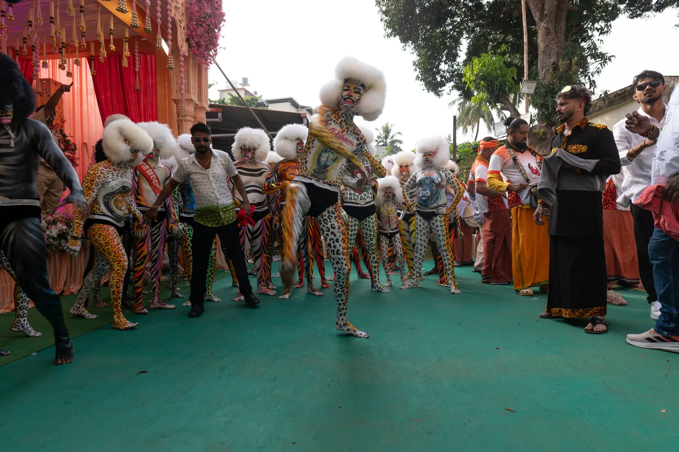 White-headpiece Pili Vesha performer dances on a green carpet surrounded by performers and onlookers.