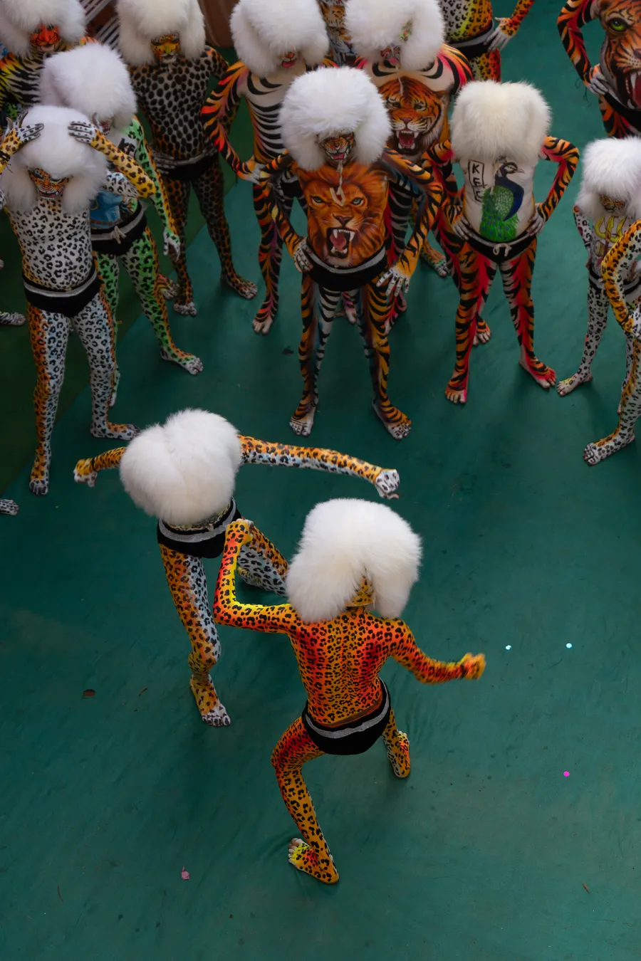 Two spotted performers in white furry headpieces dance before a group on a green carpet.